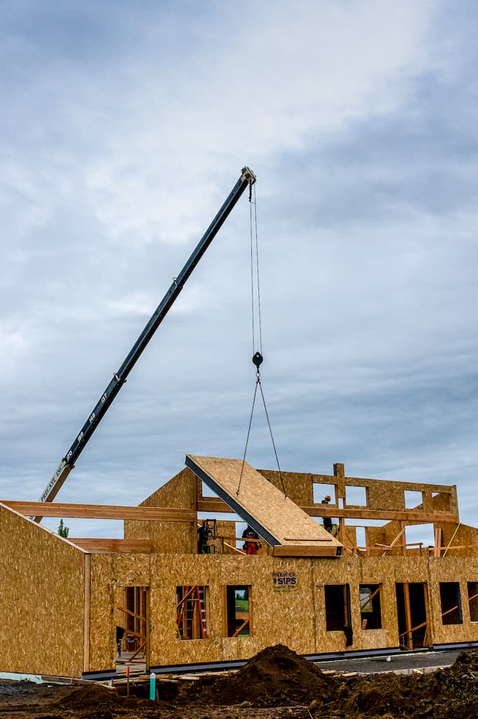 A photo of a crane placing a roof SIP on a house under construction.