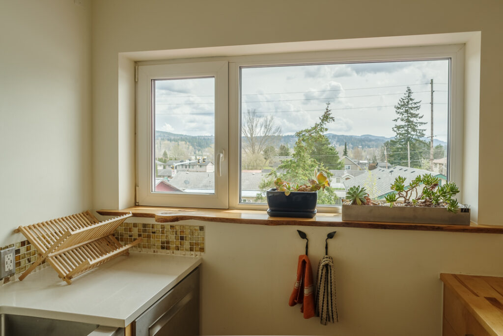 A photo of the south-facing kitchen window. Out the short but wide window you can see just the tops of houses and hills in the background.
