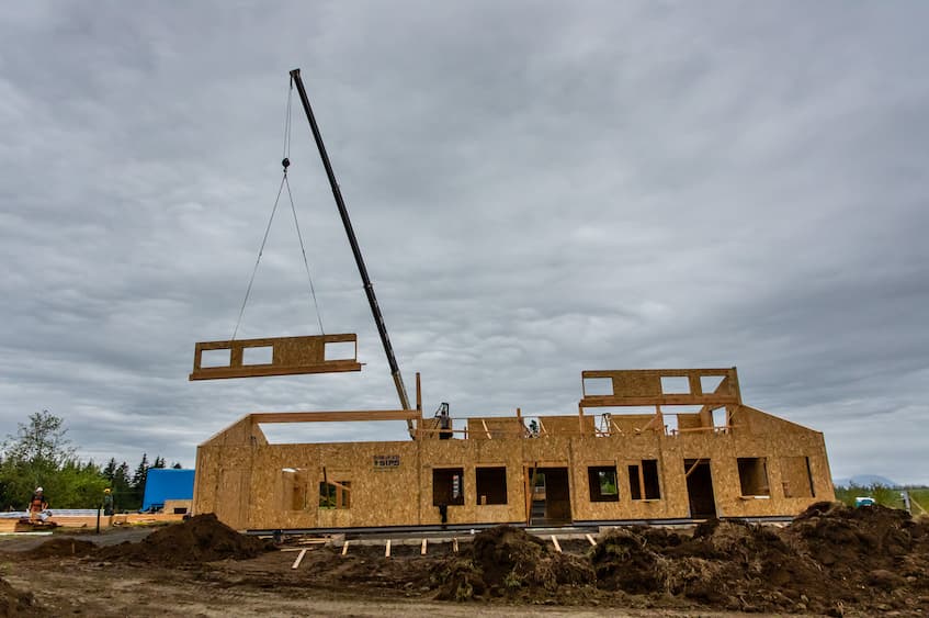 A photo of a crane moving a long wall SIP with 3 window openings that will rest on the second story creating the clearstory shell.
