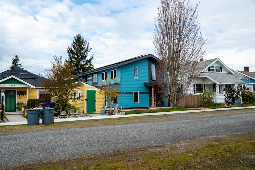 A street view of a row of colorful houses. The center blue house is a Net Zero house designed by Powerhouse Designs and built by TC Legend Homes.