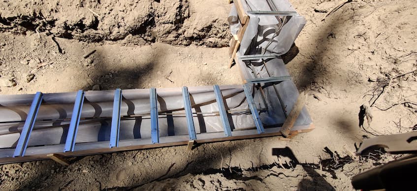 A photo of the foundation form prior to insulated concrete forms. Shown is wood form lined with a material liner, two lines of rebar running the length inside and topped with hat-channels running perpendicular.