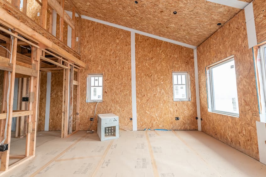 A photo of the interior of a home under construction where the SIPs have all been placed and we can see the SIP tape has been placed on all the interior joints for air sealing. Interior framing,  windows and electrical rough-in have already been installed and there is a space heater on the covered floor.