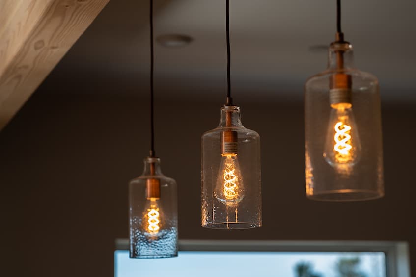 A photo of 3 light bulbs inside of 3 clear glass shades hanging from the ceiling. The bulb has twisted LED strip lights inside to make it look like an old-timey bulb.